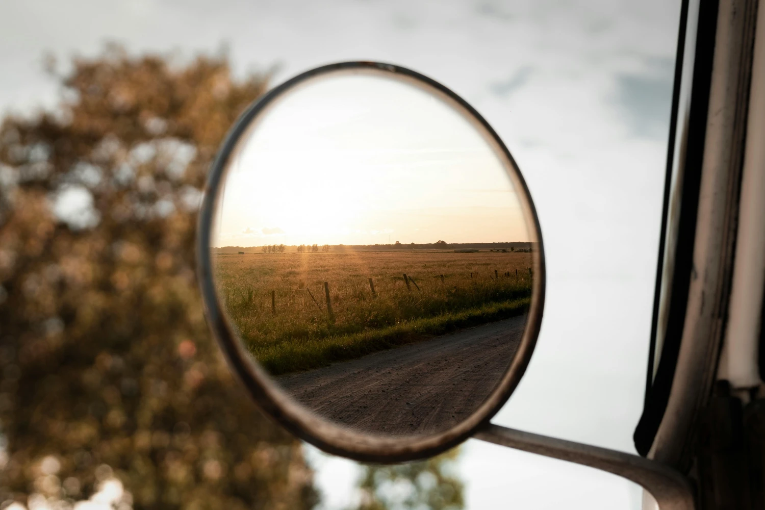 Blick auf die Wiese und den Sonnenuntergang im Spiegel eines Fahrzeugs